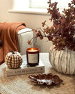 Cozy living room corner with a candle, pumpkins, and decorative items on a coffee table.