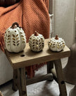 Decorative pumpkins on a small wooden stool with a cozy blanket and rustic decor in the background.