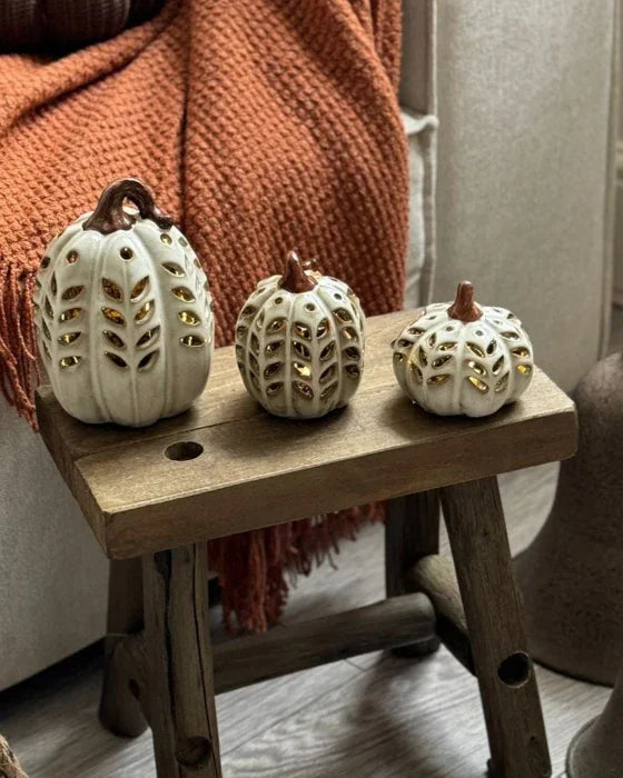 Decorative pumpkins on a small wooden stool with a cozy blanket and rustic decor in the background.