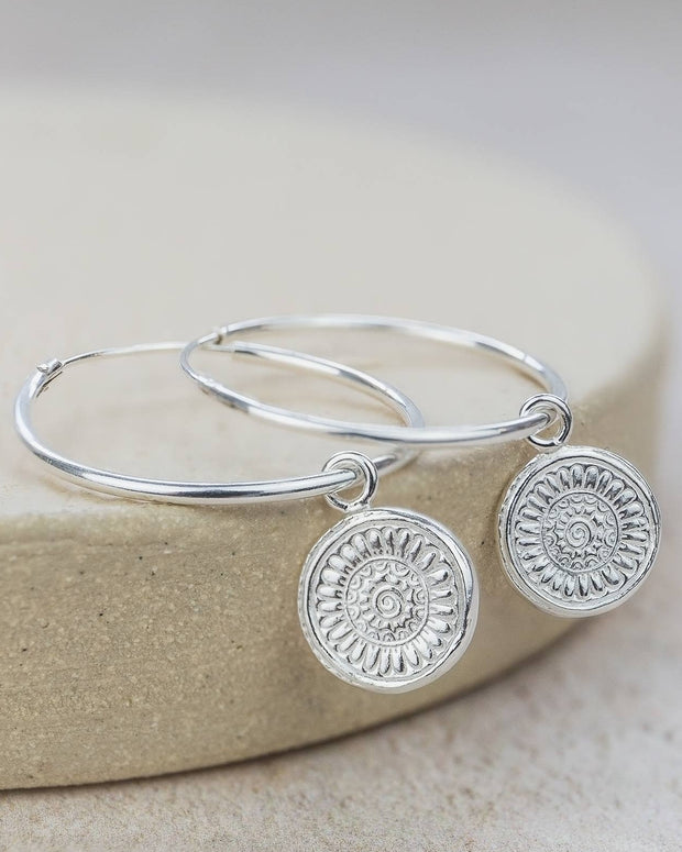 Silver hoop earrings with circular designs on a beige stone background