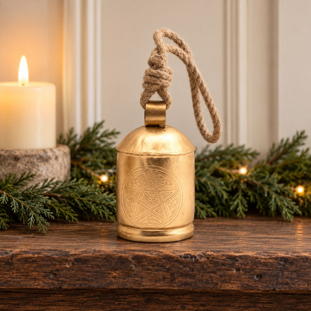 Large Brass Gold Cow Bell On Rope, gold-coloured bell on a rustic mantel beside greenery