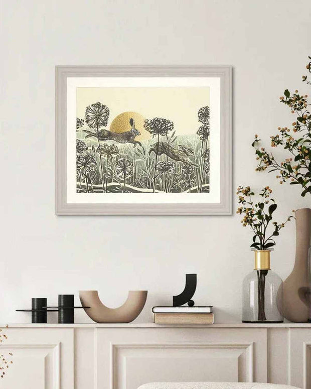 Framed artwork of deer in a forest scene on a wall above a white cabinet.