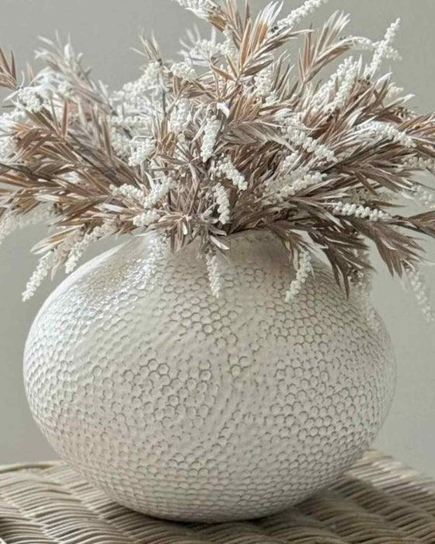 Decorative vase with textured surface and dried plants on a neutral background