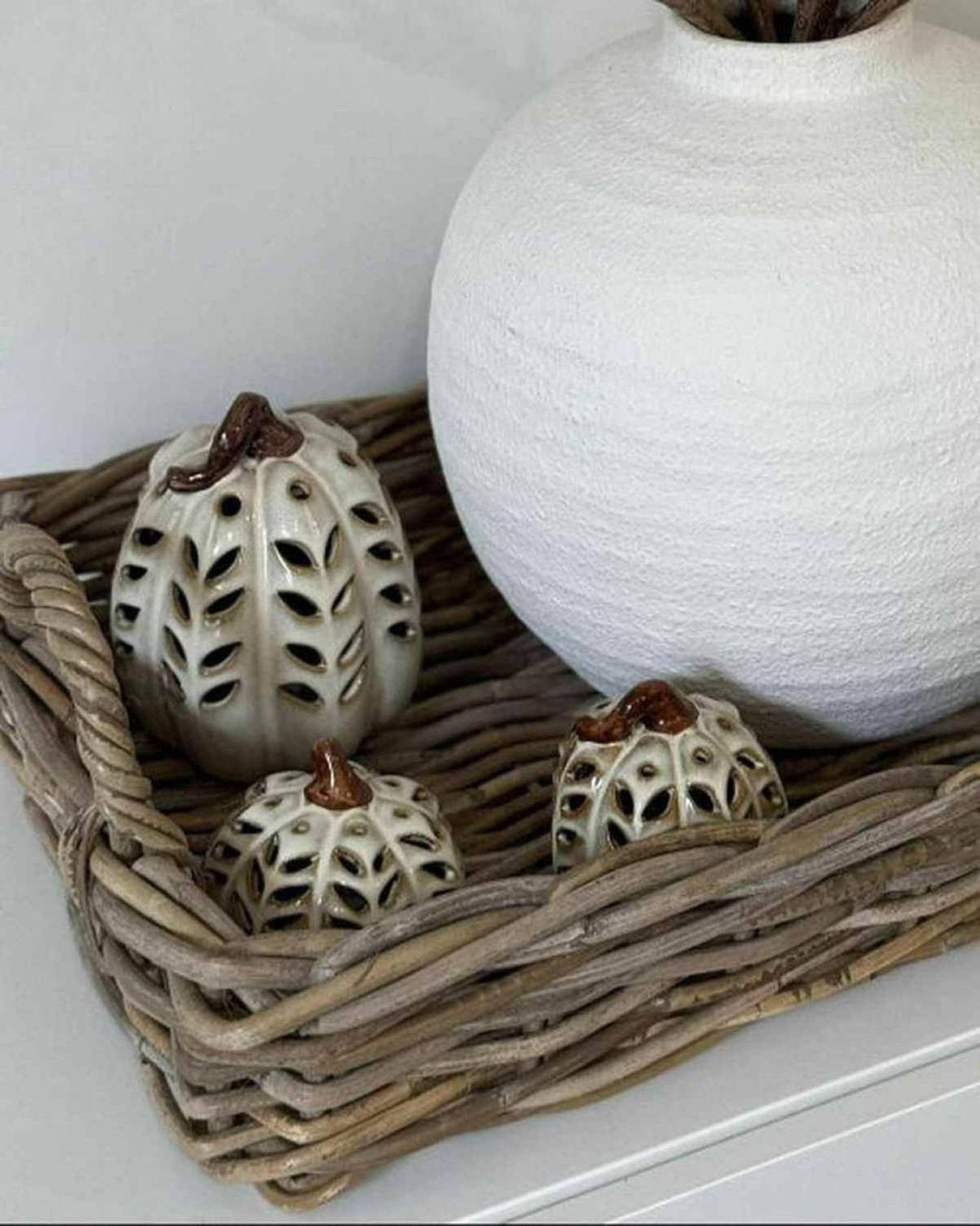 Decorative arrangement with a white textured vase, branches, and small decorative items on a woven tray.