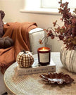 Cozy living room corner with a candle, pumpkins, and decorative items on a coffee table.