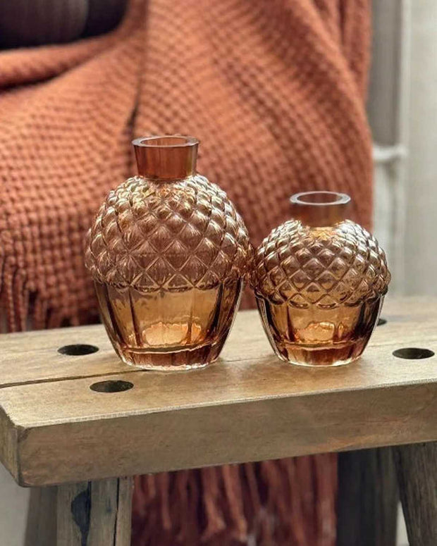 Two amber glass candle holders on a wooden surface with a textured brown blanket in the background.