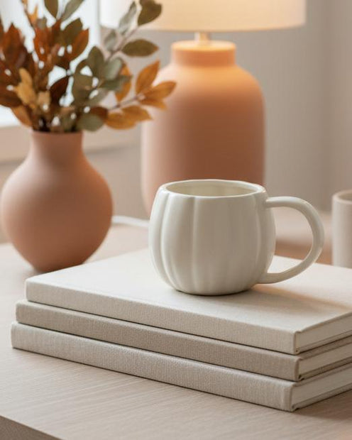 White Matt Ceramic Pumpkin Mug, white ribbed pumpkin mug on books beside autumn vases