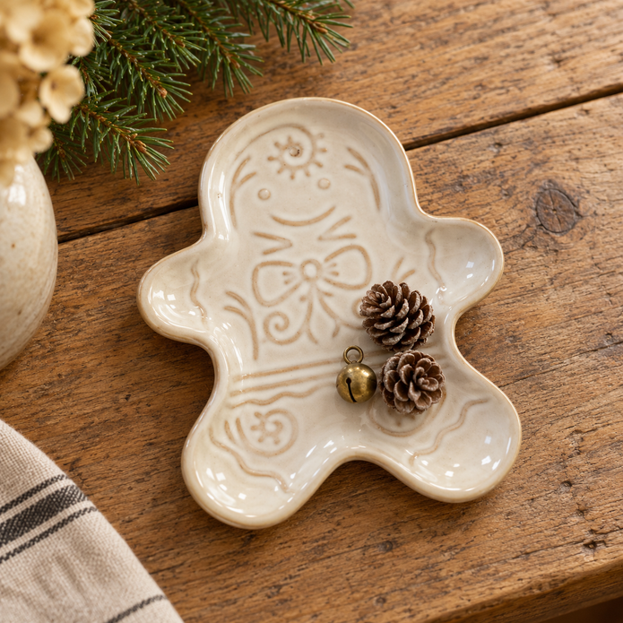 Cream ceramic gingerbread man trinket plate lying flat with pine cones and a small brass bell