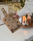 Person holding a wooden cutting board with 'Mince Pies' written on it in a festive setting.