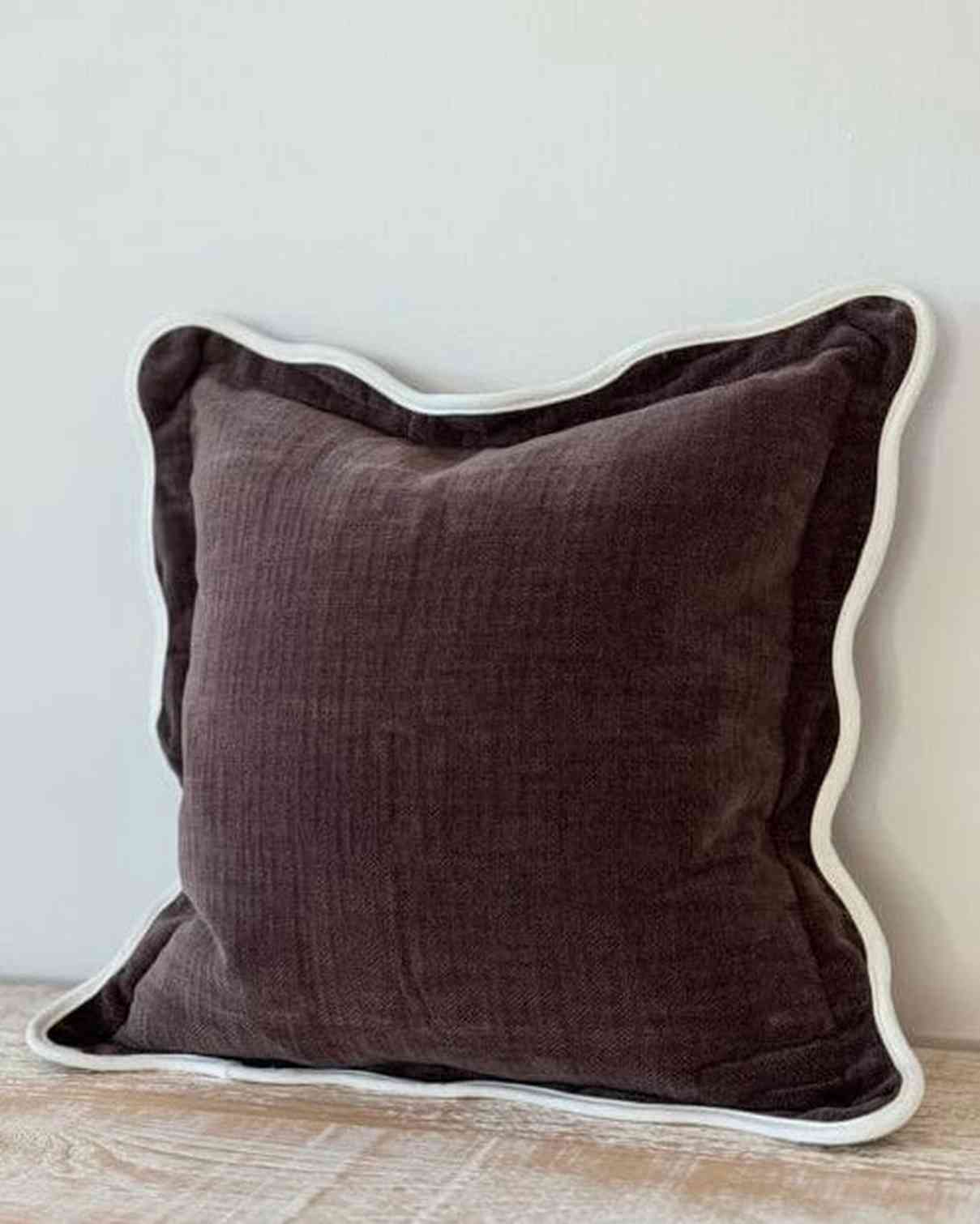 Brown pillow with white trim on a wooden surface against a light gray background