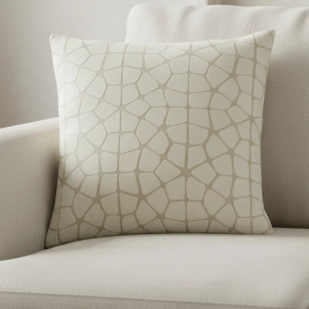 A square throw pillow featuring a textured, raised geometric pattern resembling a stone or reptile skin motif in a light beige and off-white color palette, shown against a plain white background.