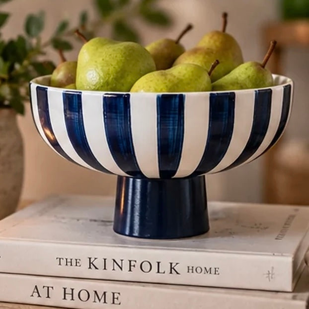Deep blue and white striped ceramic footed bowl holding green pears on a stack of books