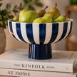 Deep blue and white striped ceramic footed bowl holding green pears on a stack of books