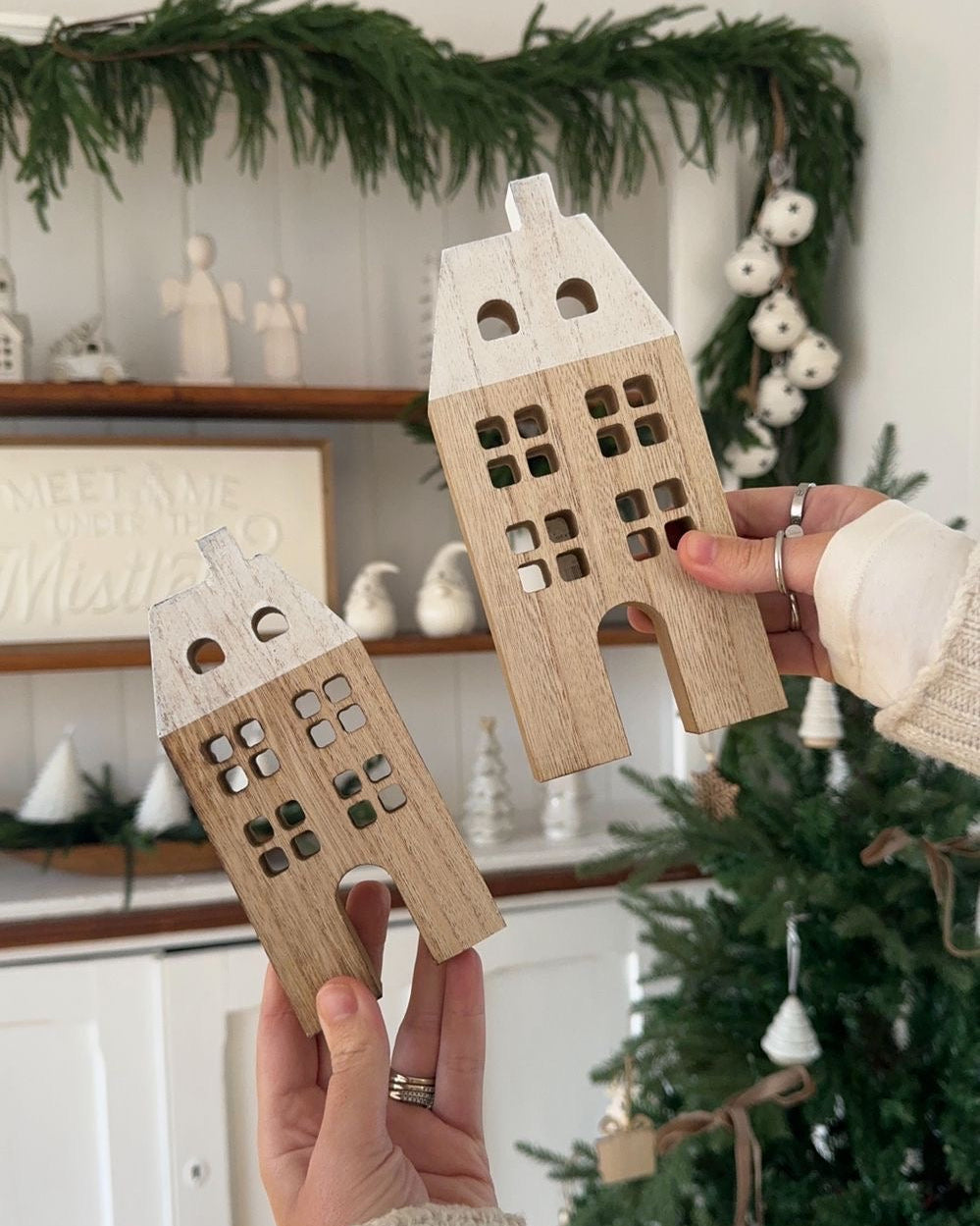 Wooden house-shaped ornaments held by a person in front of a decorated Christmas tree.