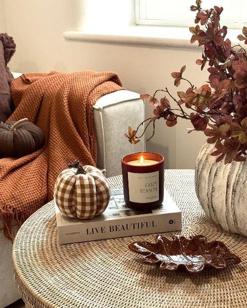 Cozy living room corner with a candle, pumpkins, and decorative items on a coffee table.
