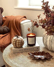 Cozy living room corner with a candle, pumpkins, and decorative items on a coffee table.