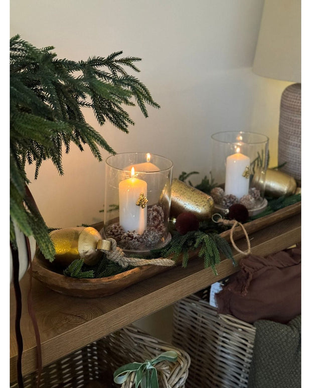 Decorative setup with candles, greenery, and a basket on a wooden surface.