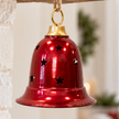 Burgundy metal bell with star openings suspended beneath a rustic mantel decorated with greenery