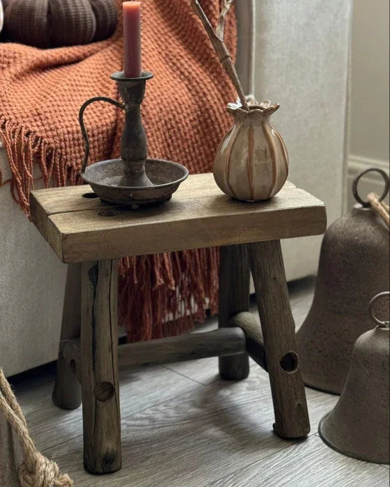 Cozy living room corner with a wooden stool, candles, and decorative items.