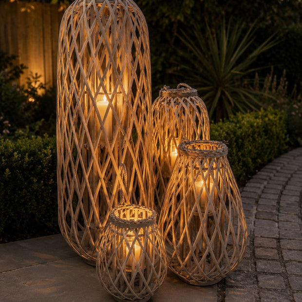 Burley Rattan Bulbous Garden Candle Lantern, grouped tall woven lanterns glowing on a garden patio at night