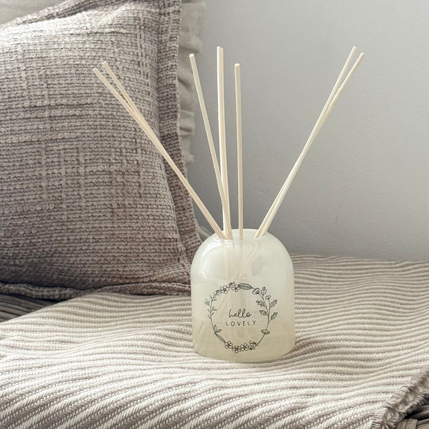 Beige Moments Clear Glass Reed Diffuser -  Hello Lovely, pale diffuser with white reeds beside grey cushions