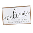 Welcome to Our Beautiful Chaos sign with black lettering on a white panel in a natural wood frame.