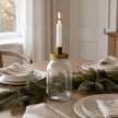 Ivory Candles In A Glass Storage Jar And Holder, clear storage jar with brass lid holding a lit taper on a dining table