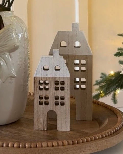 Two wooden house-shaped candle holders on a wooden surface with a blurred background.