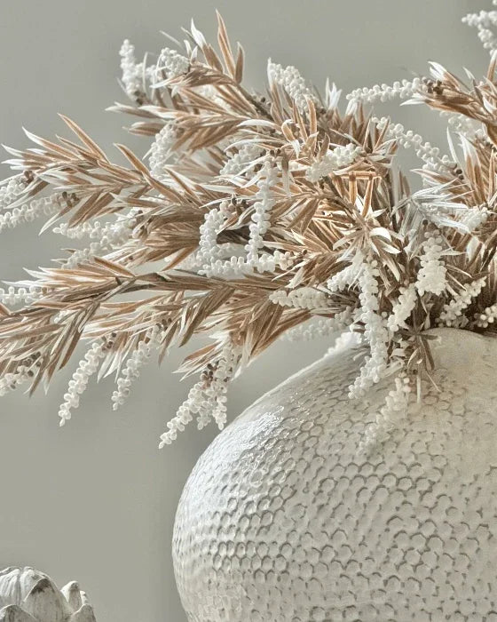 Textured vase with dried plants against a neutral background