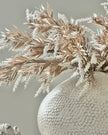 Textured vase with dried plants against a neutral background