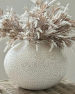 Decorative vase with textured surface and dried plants on a neutral background