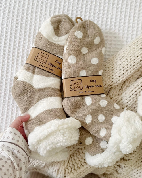 Pair of cozy slipper socks with polka dot pattern held by a hand on a textured fabric background.