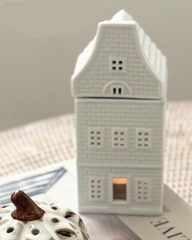 Ceramic house-shaped lantern with a small light inside on a neutral background