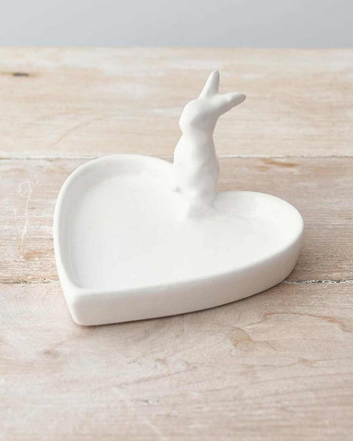 White ceramic heart-shaped trinket dish with a small deer figure on a wooden surface.