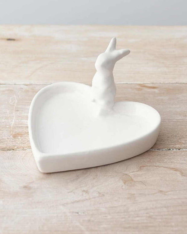 White ceramic heart-shaped trinket dish with a small deer figure on a wooden surface.