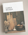 Book titled 'Family Recipes' with wooden cutting boards and bowls on a wooden shelf.