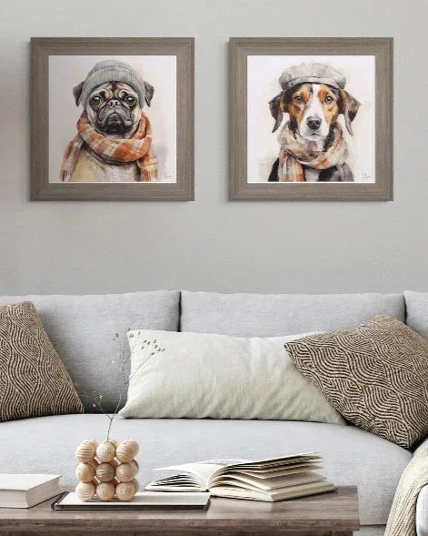 Two framed paintings of dogs wearing hats and scarves above a gray sofa with decorative pillows.