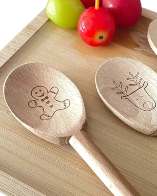 Wooden spoons with engraved designs on a wooden surface with fruits in the background