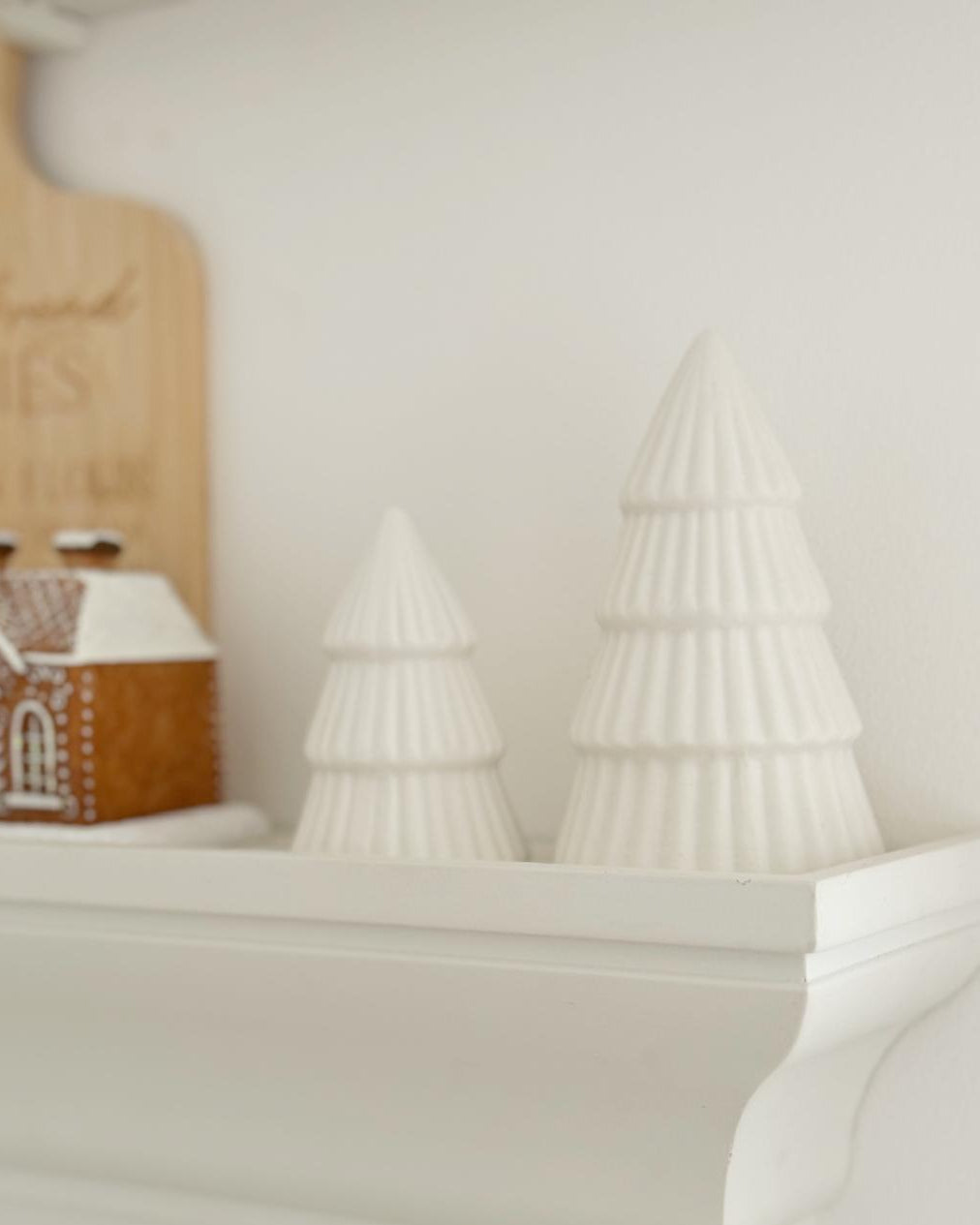 Decorative Christmas trees on a mantel with a gingerbread house.
