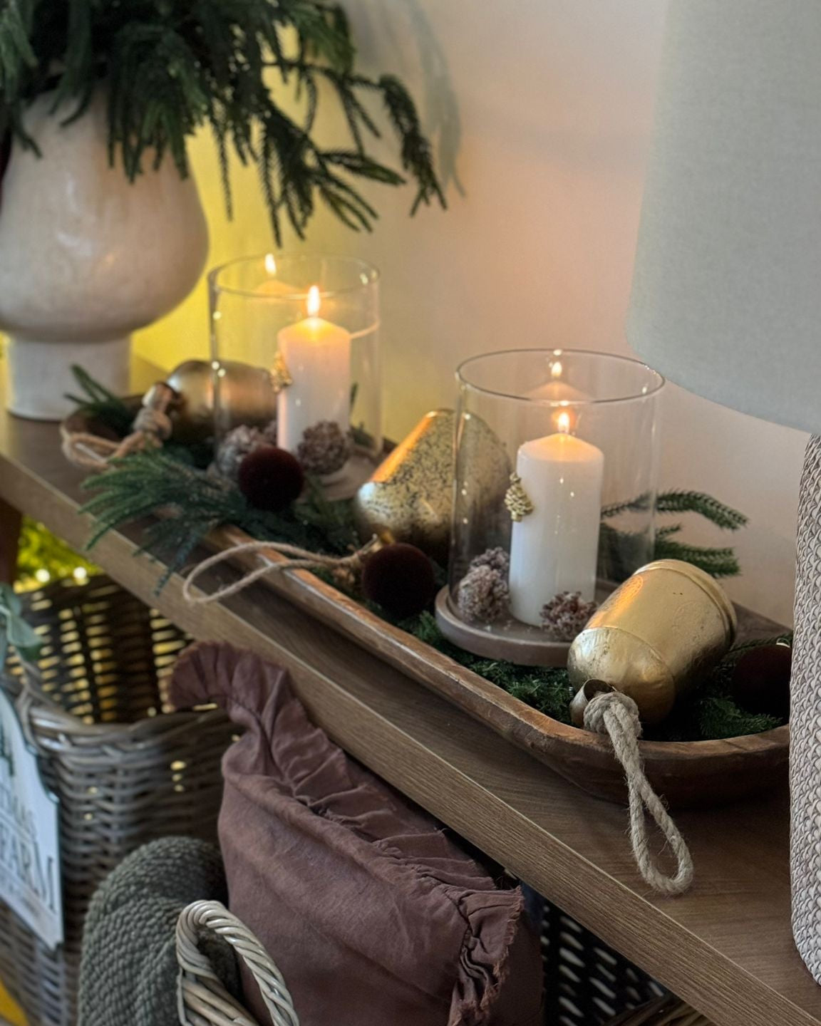 Decorative rustic long wooden bowl setup with candles, greenery, and a basket on a shelf.