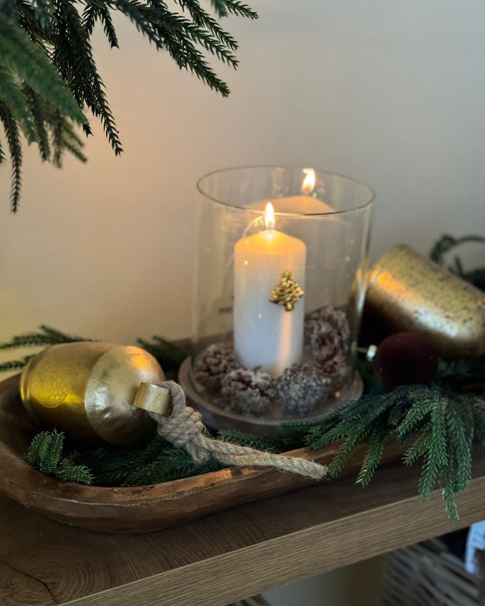 Decorative setup with a candle, bottle, and greenery on a wooden surface.