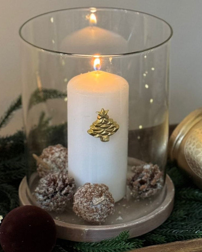 Decorative candle in a glass holder with pinecones and a wooden box on a neutral background