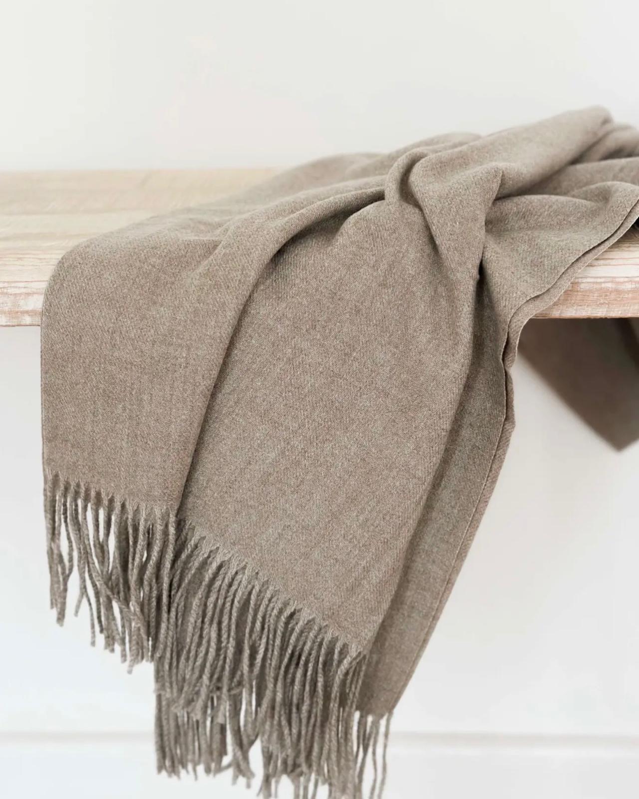 Beige and brown fine knit tasseled throw blanket by Ellenvale Trade for soft furnishings, shown draped over a cozy sofa.