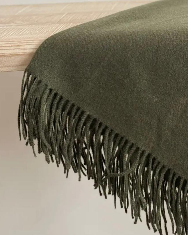 Olive green Della fine knit tasselled throw blanket from Ellenvale Trade, showing soft, textured fabric with fringed edges.