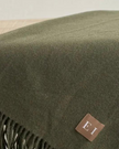 Olive green Della fine knit tasselled throw blanket by Ellenvale Trade, showing soft, textured fabric with decorative tassels.