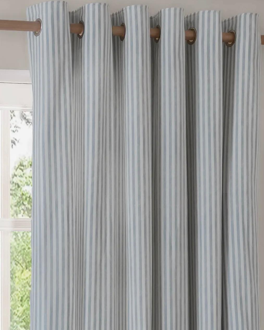 Riva Home ocean blue striped blackout eyelet curtains hanging in a window, soft furnishings with black and blue striped design.