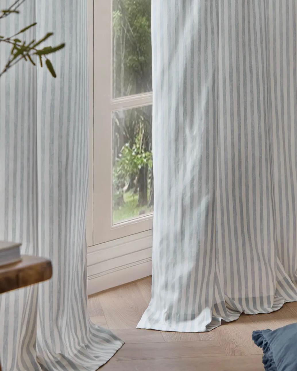 Riva Home Yard Ocean Blue striped blackout eyelet curtains hanging in a window, soft furnishings with bold blue and black stripes.