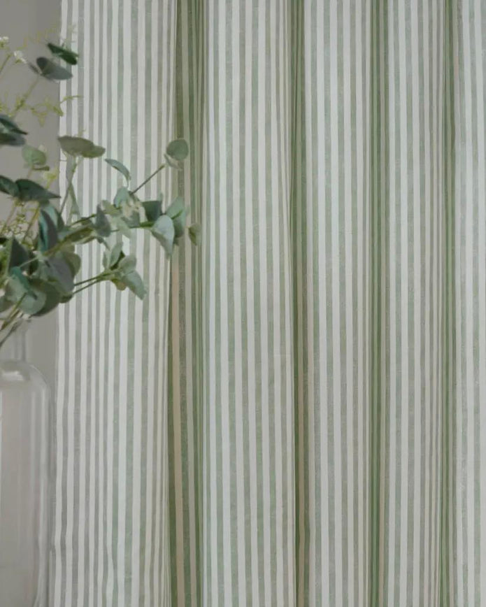 Yard Sage Green and black striped blackout eyelet curtains from Riva Home hanging in a living room window.