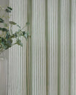 Yard Sage Green and black striped blackout eyelet curtains from Riva Home hanging in a living room window.