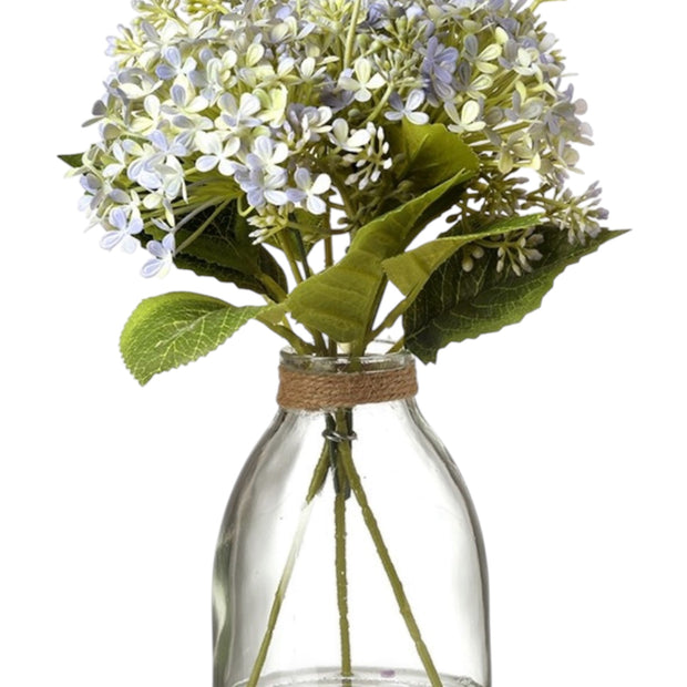 Artificial pale blue flower arrangement in a clear glass vase by Heaven Sends, showcasing delicate blooms and lush greenery.
